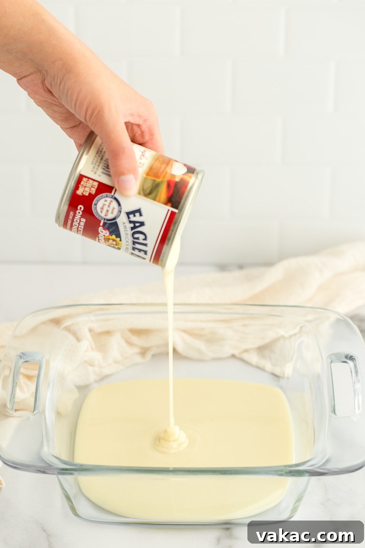 A can of sweetened condensed milk being carefully poured into a clear glass baking dish, the single key ingredient for homemade dulce de leche.