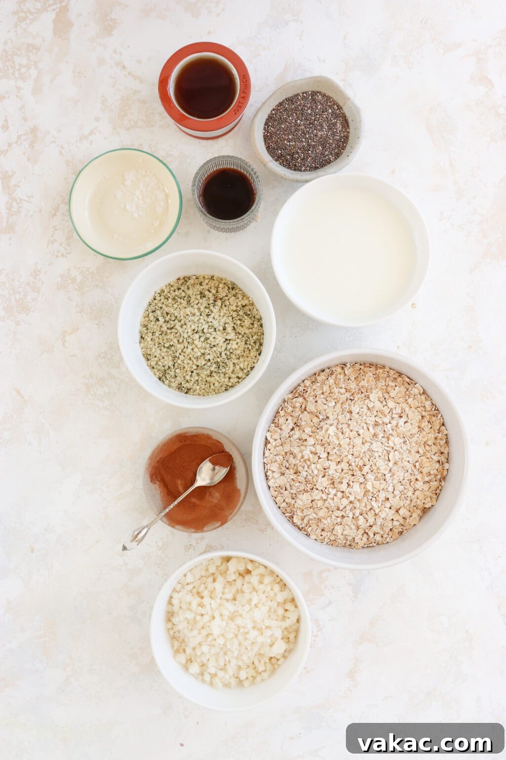 Make-Ahead Cinnamon Roll Overnight Oats 3 A beautiful flat lay image showcasing all the wholesome ingredients required for meal prep cinnamon roll overnight oats: quick oats, hemp hearts, chia seeds, vanilla extract, milk, maple syrup, salt, ground cinnamon, and the secret ingredient, cauliflower rice, neatly arranged in small white and clay bowls on a rustic surface.