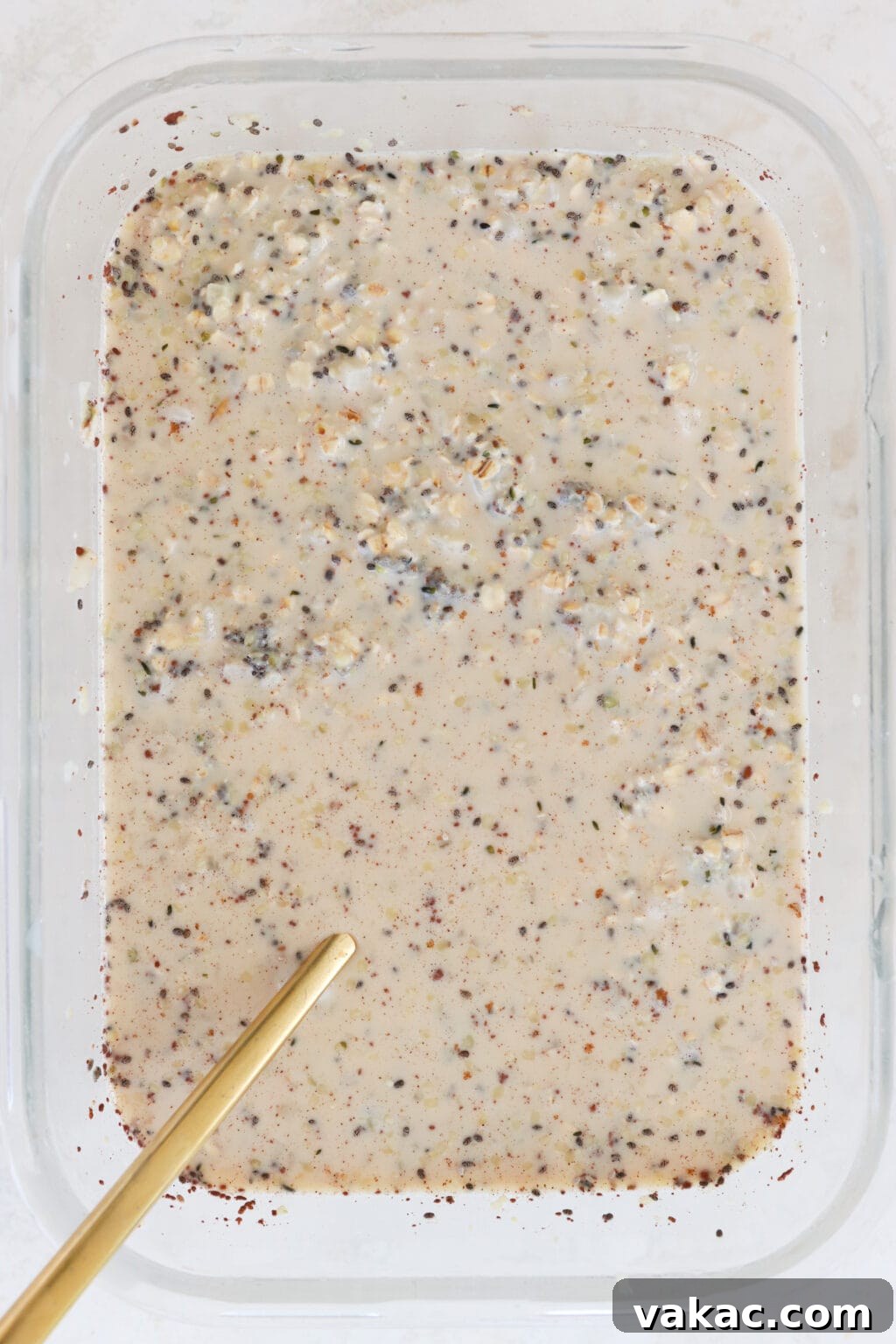 Make-Ahead Cinnamon Roll Overnight Oats 5 A glass container filled with the perfectly mixed ingredients for cinnamon roll overnight oats, including quick oats, hemp hearts, chia seeds, vanilla extract, milk, maple syrup, salt, ground cinnamon, and cauliflower rice, showcasing the creamy consistency before setting.