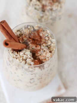 Two glasses on a white surface filled with meal prep cinnamon roll overnight oats with two cinnamon sticks