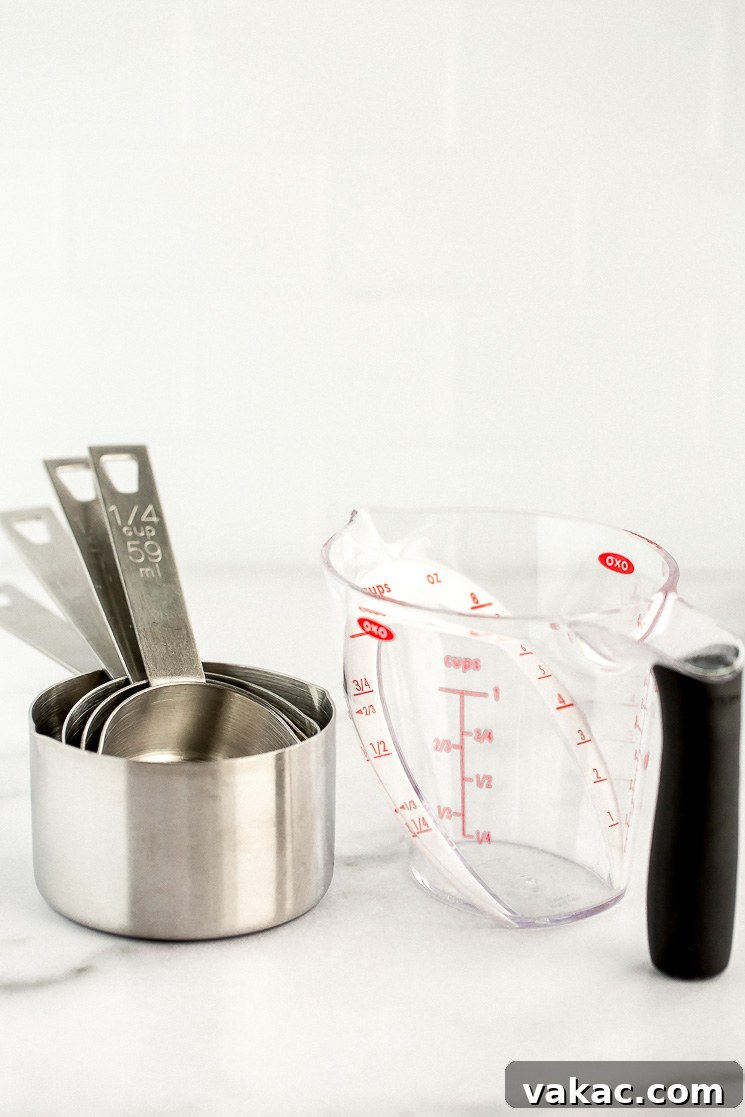 The Ultimate Baking Tool Guide 4 A set of metal measuring cups and a plastic angled liquid measuring cup sitting on a marble counter.