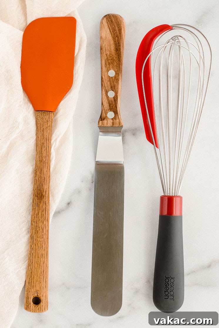 The Ultimate Baking Tool Guide 5 A rubber spatula, an icing spatula, and a whisk resting on top of a marble counter.