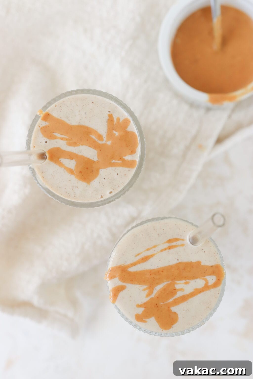 Two glasses filled with healthy peanut butter banana smoothie with a bowl of melted peanut butter on the side