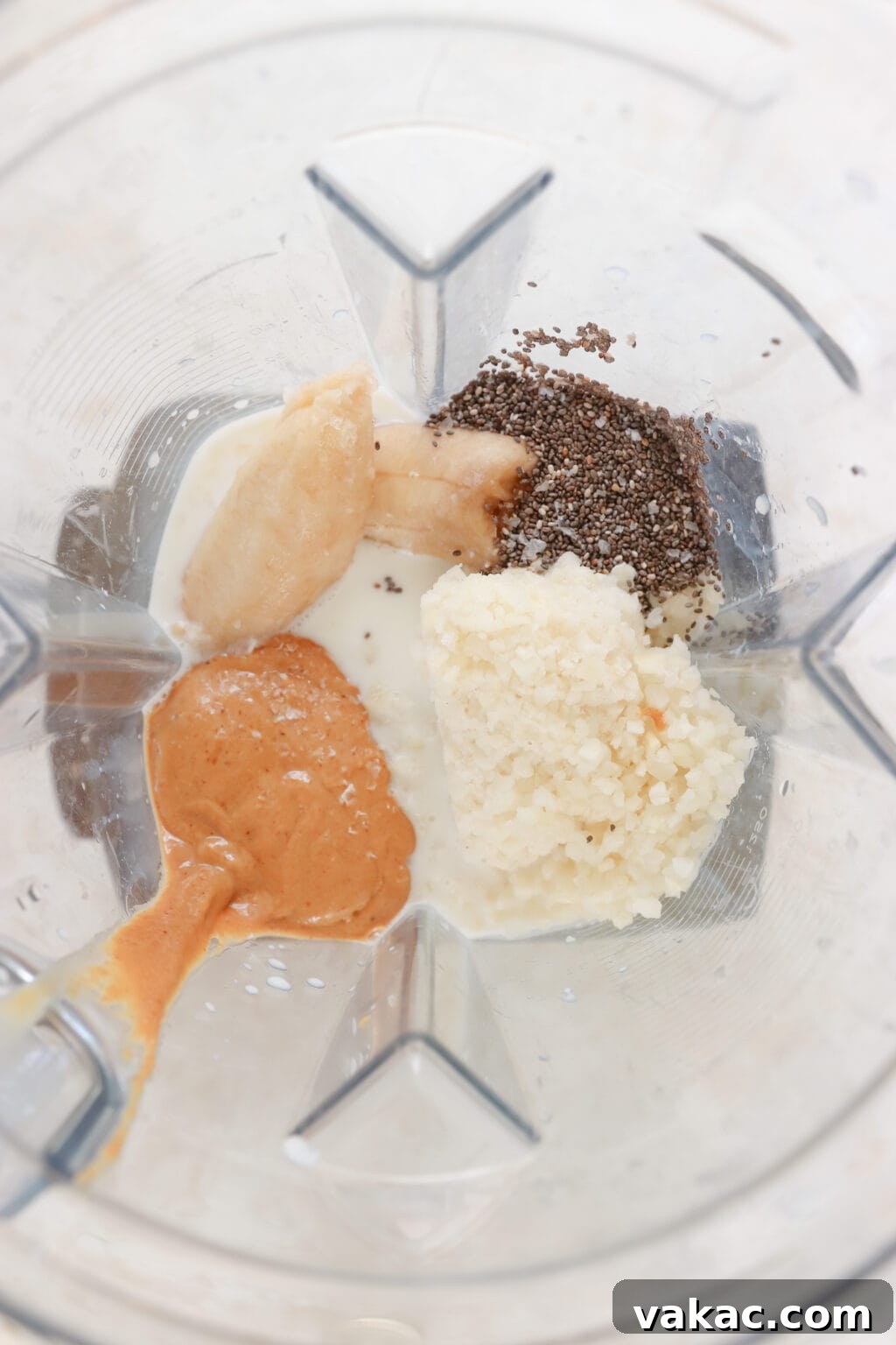 Ingredients for a healthy peanut butter banana smoothie in a blender, including banana, peanut butter, cauliflower rice, milk, and chia seeds