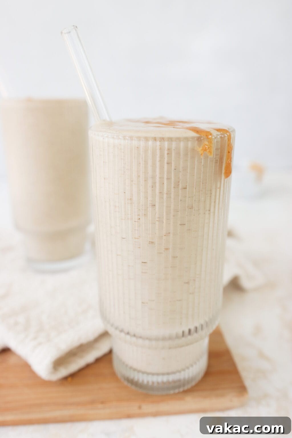 Two glasses filled with healthy peanut butter banana smoothie with a bowl of melted peanut butter on the side