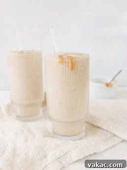 Two glasses filled with healthy peanut butter banana smoothie with a bowl of melted peanut butter on the side