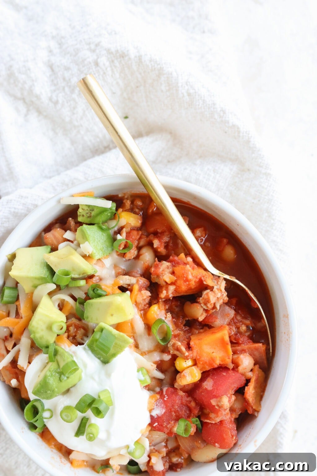 Comforting Slow Cooker Sweet Potato and Turkey Chili 8 A single white bowl of Slow Cooker Sweet Potato and Turkey Chili, garnished with vibrant green cilantro, set against a classic white tablecloth, ready to be enjoyed.