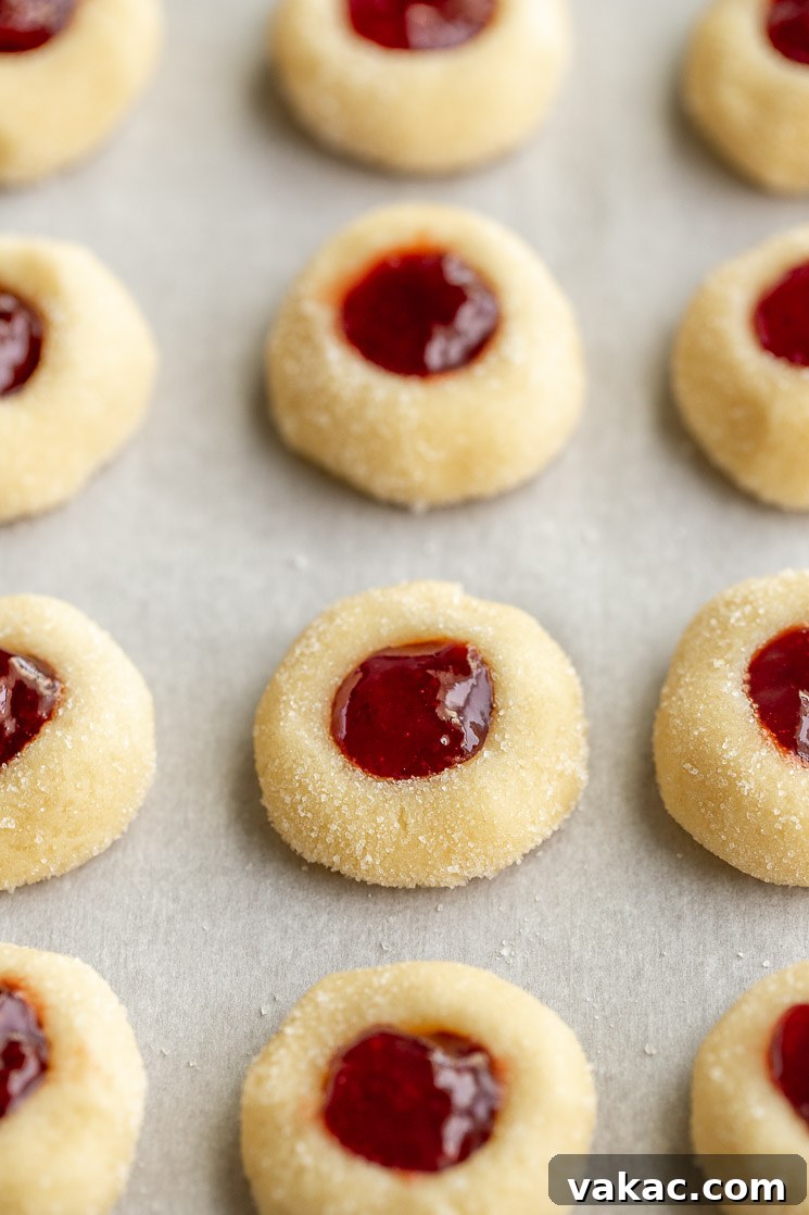 Sweet Impressions 3 A batch of unbaked thumbprint cookies filled with jam lined up on a piece of parchment paper.