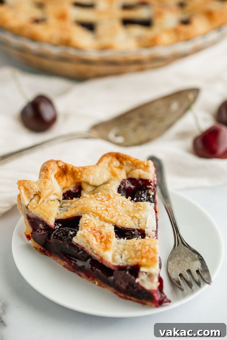 A perfectly baked slice of homemade cherry pie, showcasing its flaky golden crust and vibrant, sweet cherry filling, served on a white plate with an antique silver fork.
