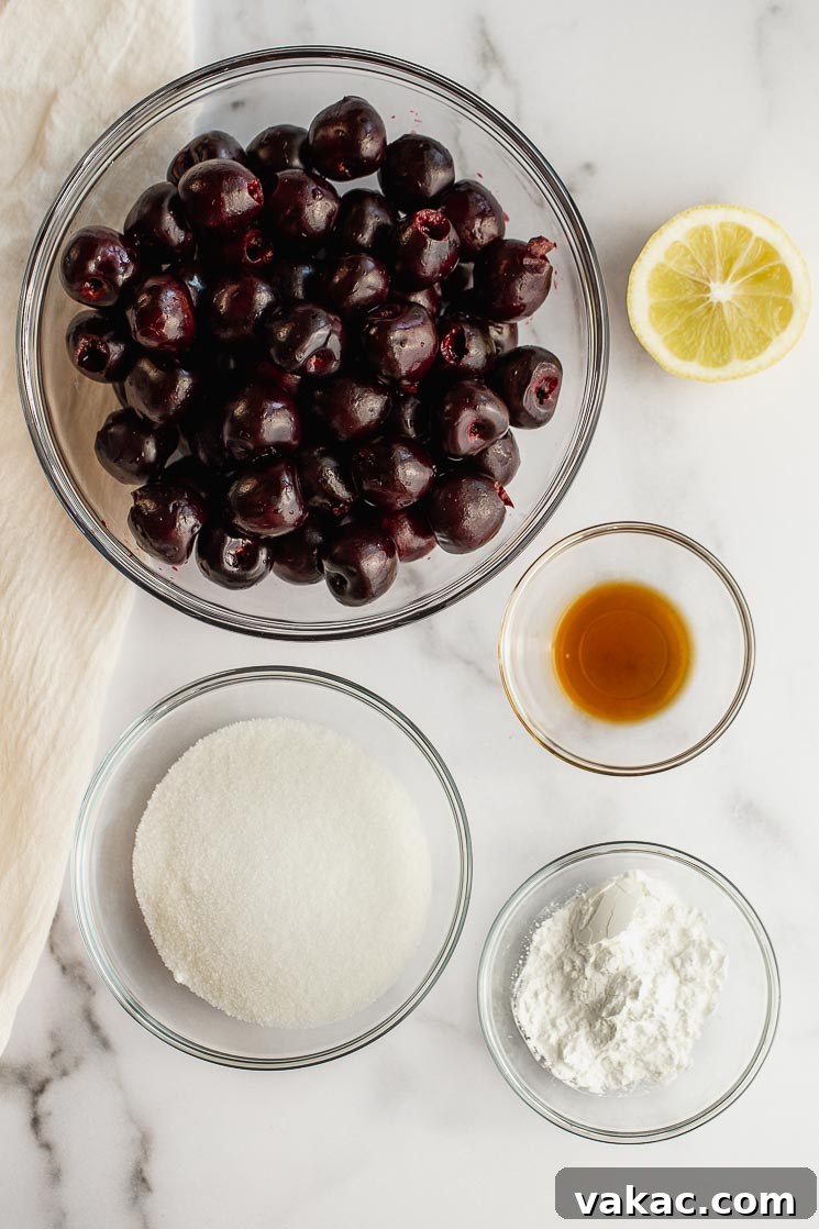 Fresh cherry pie ingredients laid out on a clean marble surface, including pitted and halved cherries, granulated sugar, cornstarch, lemon, and vanilla extract.