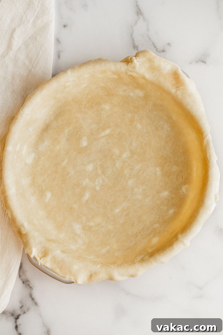 A perfectly crimped homemade pie crust resting in a glass pie plate on a polished marble surface, ready for filling.