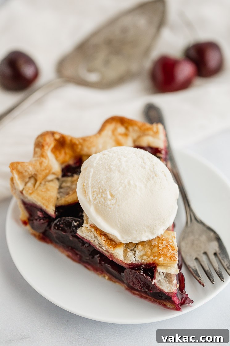 A delectable slice of homemade cherry pie topped with a scoop of vanilla ice cream, served on a white plate, ready to be enjoyed.