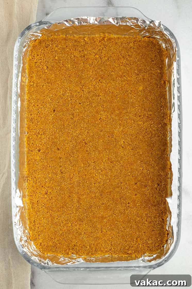 Ultimate Layered Indulgence 3 A 9x13 inch baking pan lined with aluminum foil, showing a perfectly pressed graham cracker crust base.