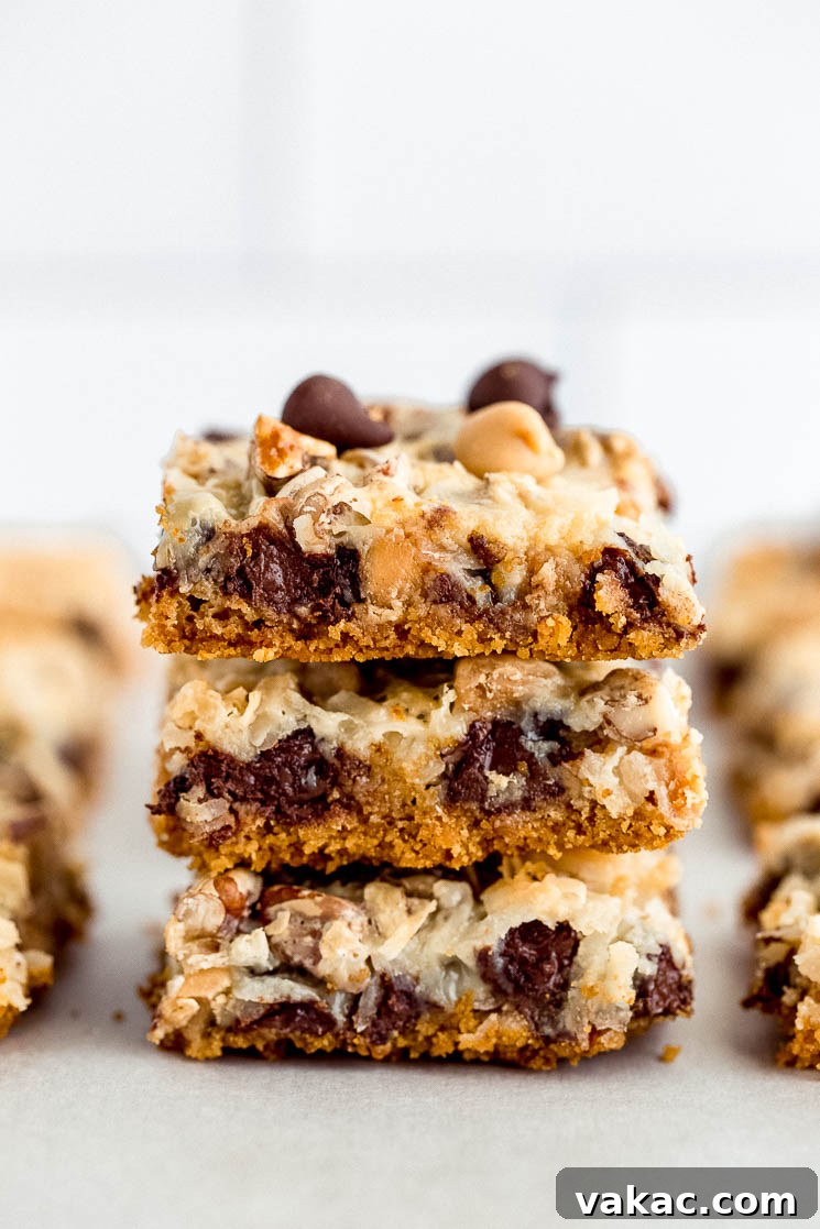 Ultimate Layered Indulgence 5 A delightful stack of 7 layer magic cookie bars, perfectly cut and arranged on parchment paper, ready to be enjoyed.