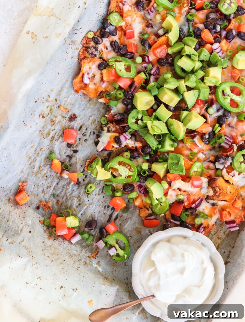 Healthy Sweet Potato Nachos with Black Beans and Bell Peppers 7 Partially eaten Healthy Black Bean & Bell Pepper Sweet Potato Nachos on a baking sheet with parchment paper and a small bowl of sour cream