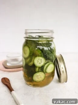 Apple Cider Vinegar Cucumber Pickles with Dill in a pickle jar with a wooden spoon and glass bowl beside the jar