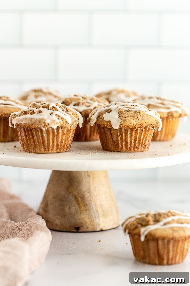 Homemade Apple Delights 2 Apple muffins sitting on top of a marble cake stand, showcasing their golden-brown tops and crumbly streusel.