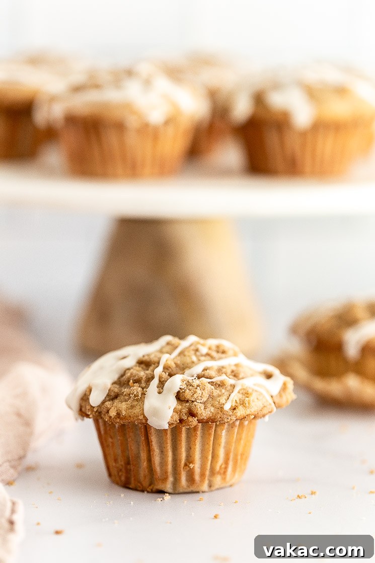 Homemade Apple Delights 5 A close-up of a single apple muffin, showcasing its delicate crumb, tender apple pieces, and golden-brown streusel, with more muffins on a cake stand in the background.