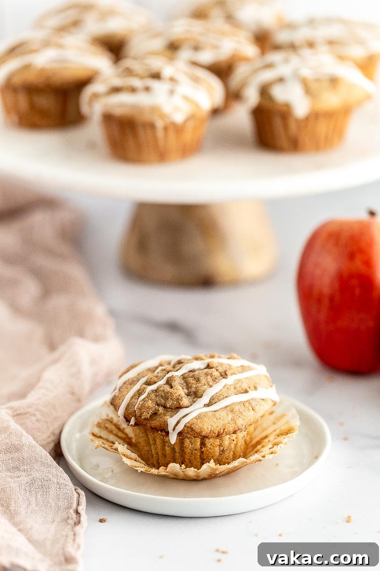 Homemade Apple Delights 6 A close-up of a single apple muffin on a white plate, with the paper liner peeled away to reveal its moist interior and apple chunks.