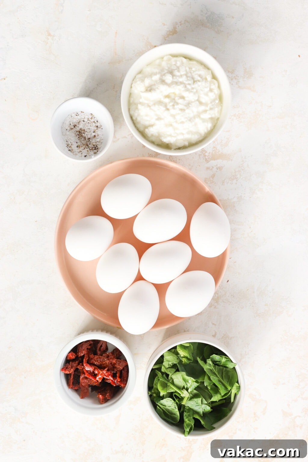 Savory Spinach, Cottage Cheese, and Sun-Dried Tomato Egg Bites 3 Fresh ingredients laid out for Egg Bites with Cottage Cheese, Spinach & Sun-dried Tomatoes, including whole eggs, a tub of cottage cheese, salt and pepper shakers, fresh spinach leaves, and diced sun-dried tomatoes