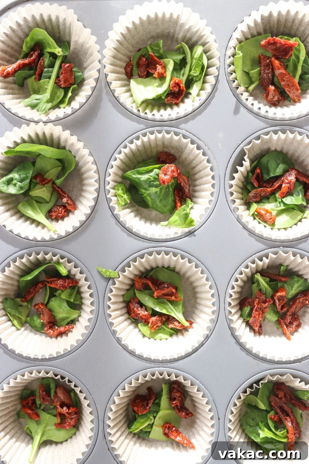 Savory Spinach, Cottage Cheese, and Sun-Dried Tomato Egg Bites 6 A muffin tin lined with baking cups, filled with chopped spinach and sun-dried tomatoes, ready for the egg mixture