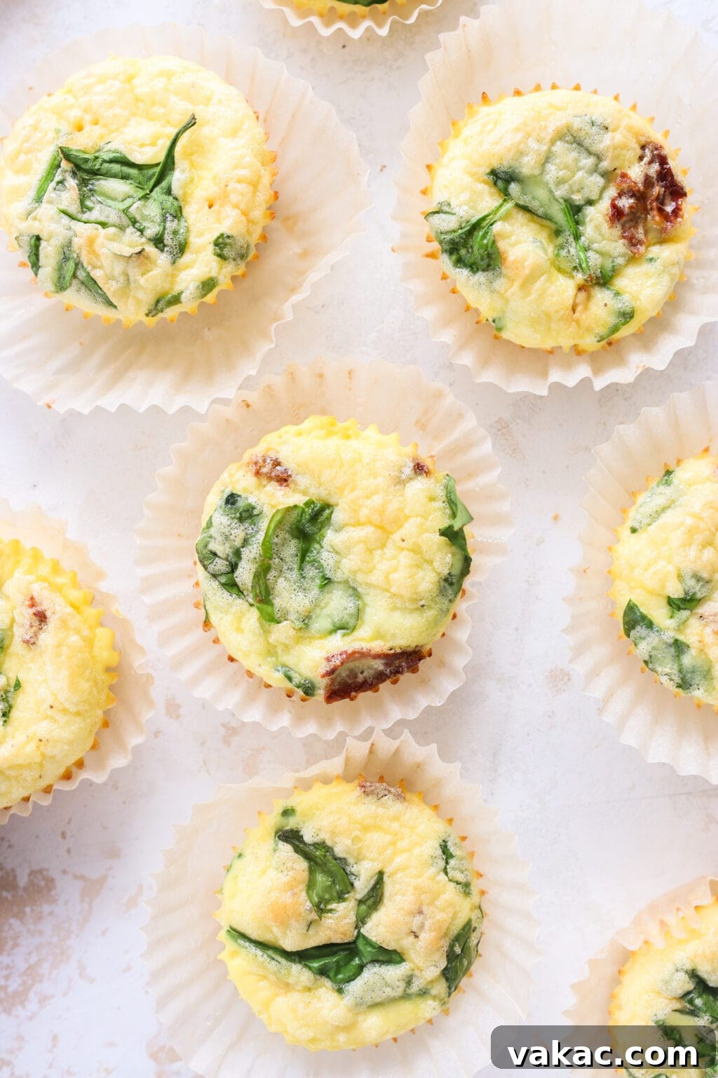 Savory Spinach, Cottage Cheese, and Sun-Dried Tomato Egg Bites 8 A selection of freshly baked Egg Bites with Cottage Cheese, Spinach & Sun-dried Tomatoes in parchment paper baking cups, arranged on a rustic wooden table