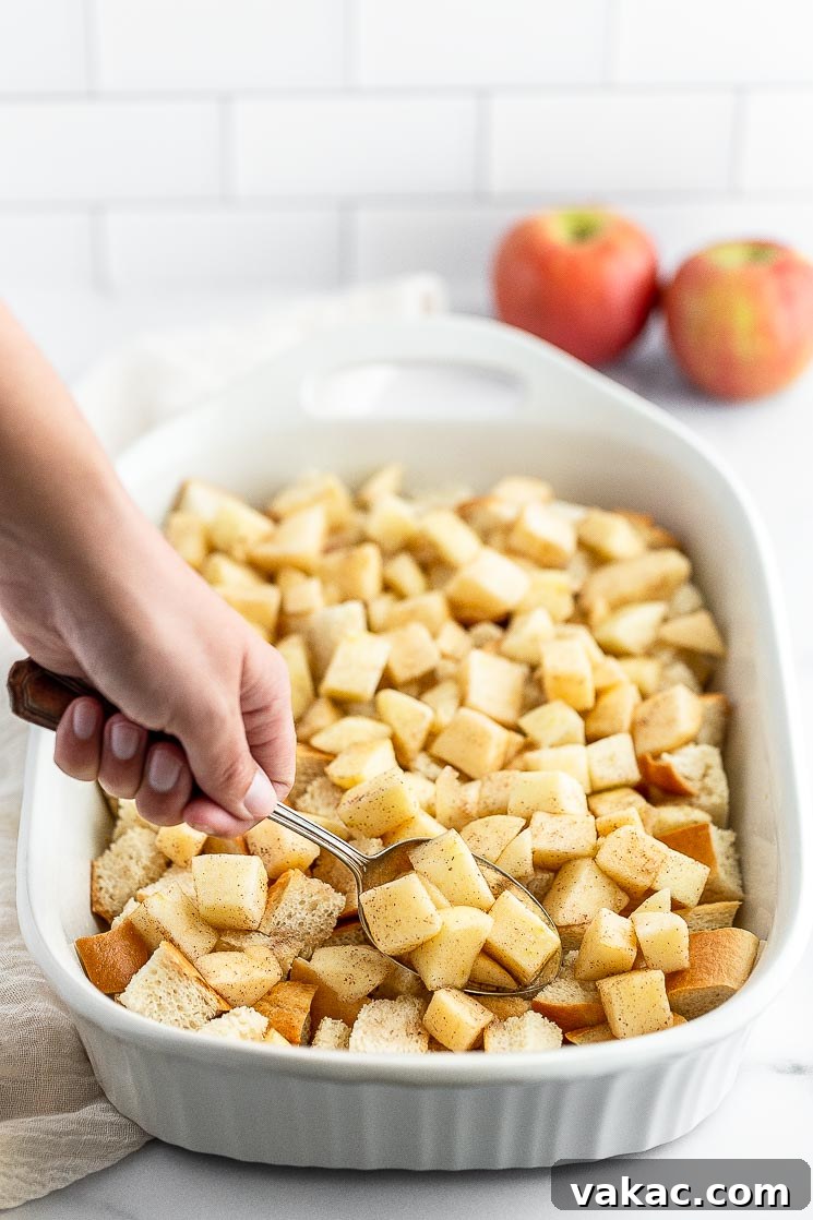 Cinnamon Apple Streusel French Toast Bake 3 Chopped apples being adding on top of cubed bread in a baking pan, ready for the next layer of bread.