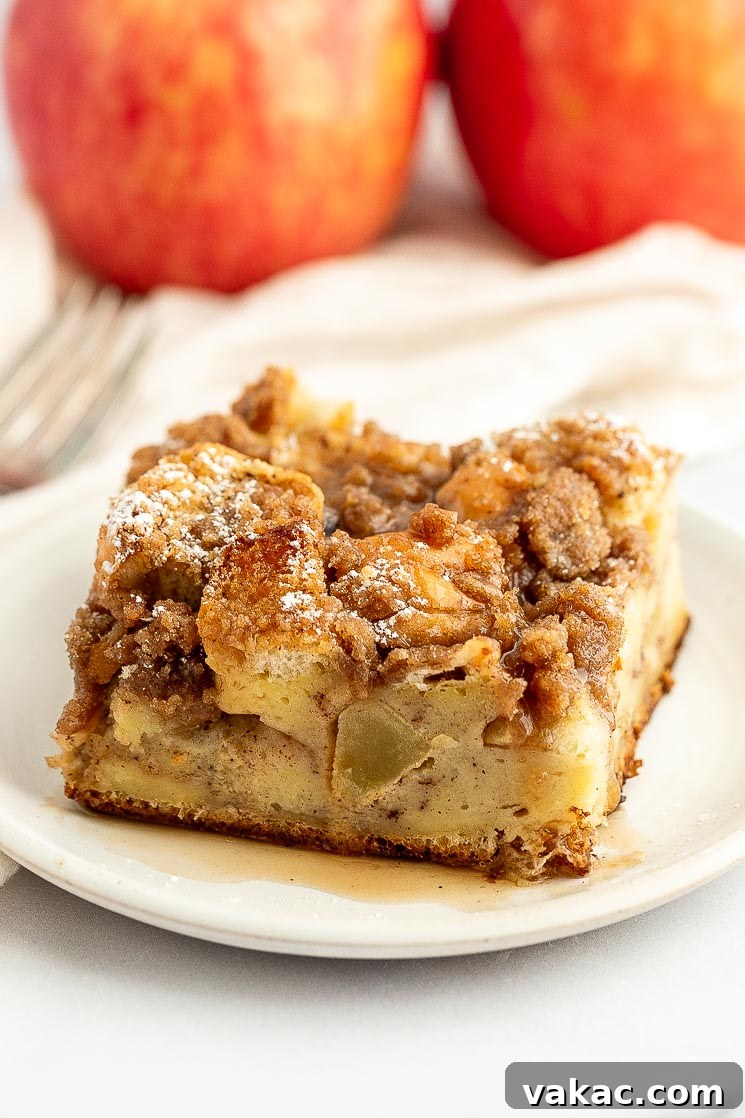 Cinnamon Apple Streusel French Toast Bake 7 A close-up slice of apple french toast casserole topped with a generous drizzle of maple syrup on a white plate, highlighting the streusel.