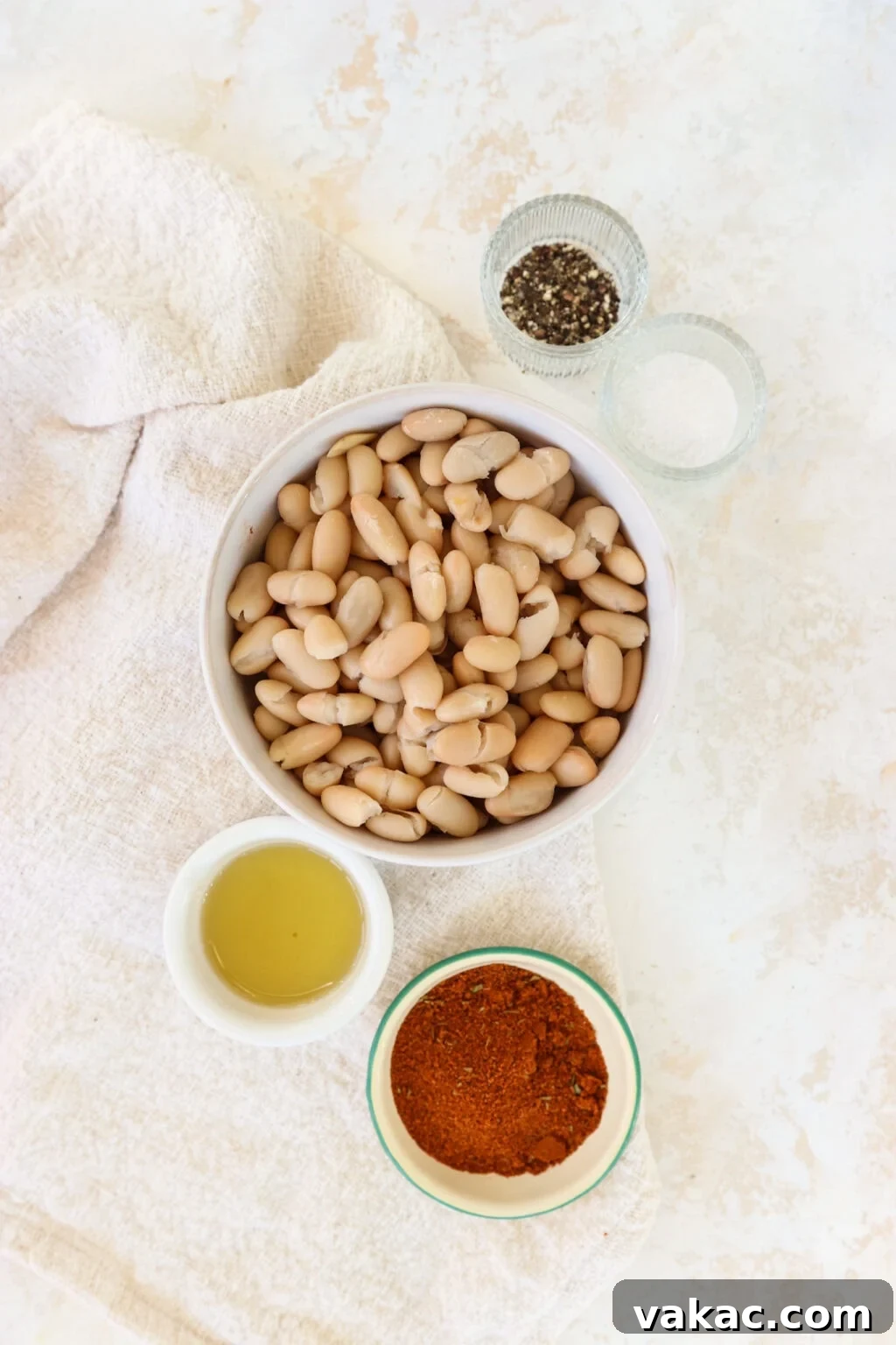 Make-Ahead Cajun Roasted White Beans 3 Ingredients for prep ahead roasted cajun spice white beans, including white kidney (cannellini) beans, avocado oil, Cajun seasoning, garlic, salt, and pepper laid out on a wooden board.