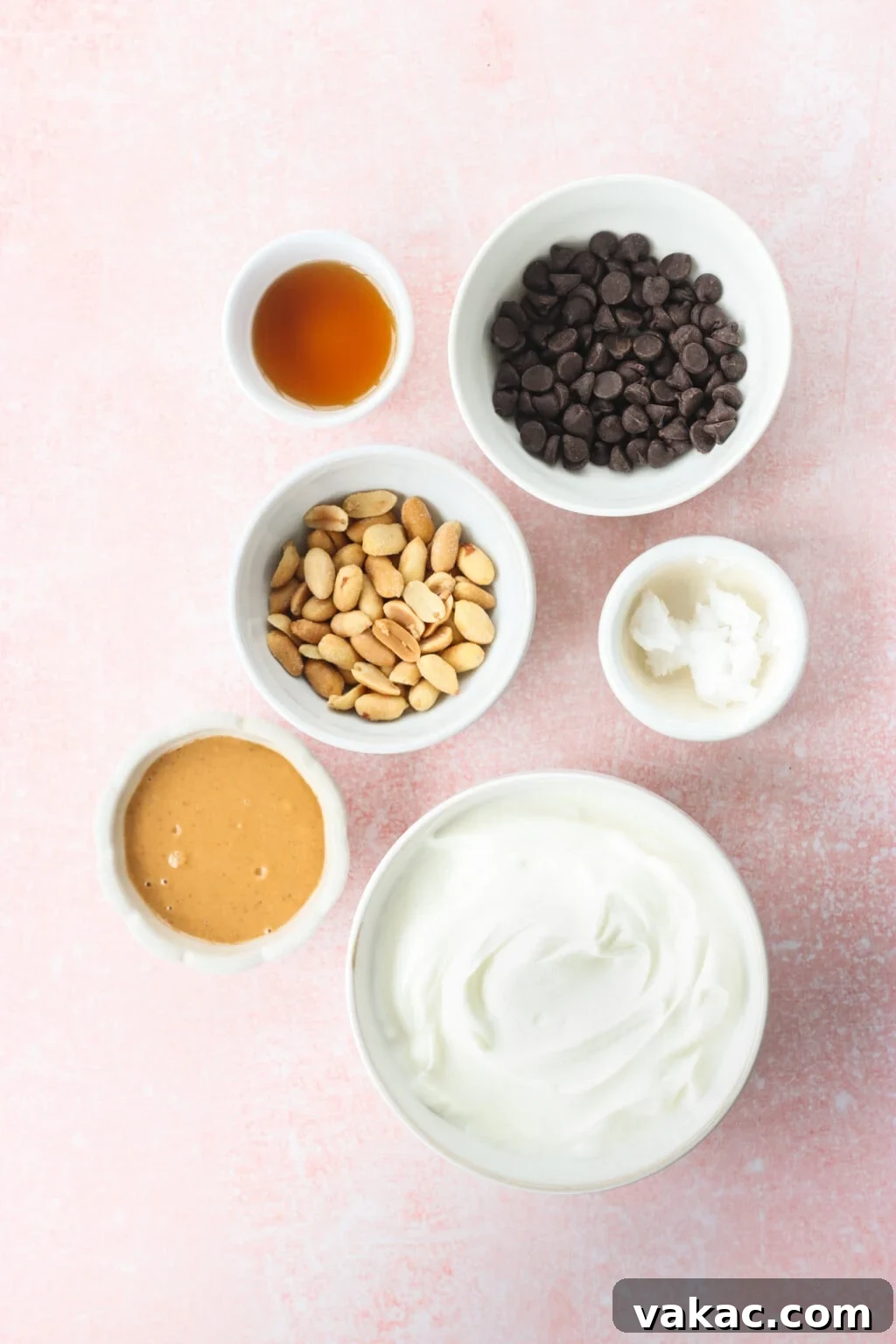 Creamy Peanut Butter and Greek Yogurt Cups with Chocolate Crunch 4 Ingredients for Peanut Butter & Greek Yogurt Cups with Magic Chocolate Shell in small white bowls on a pink marble counter, including Greek yogurt, smooth peanut butter, maple syrup, salted toasted peanuts, chocolate, coconut oil