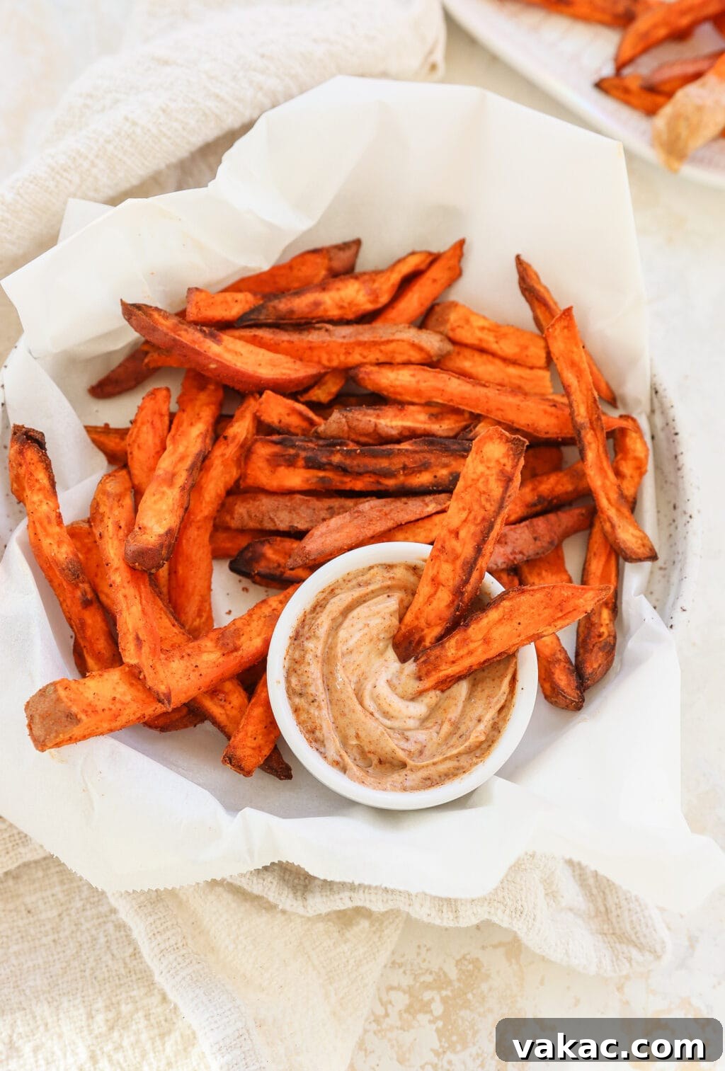 The Ultimate 4-Ingredient Crispy Air Fryer Sweet Potato Wedges 2 Golden brown crispy air fryer sweet potato wedges served in a white bowl with parchment paper and a side dip, ready to be enjoyed.