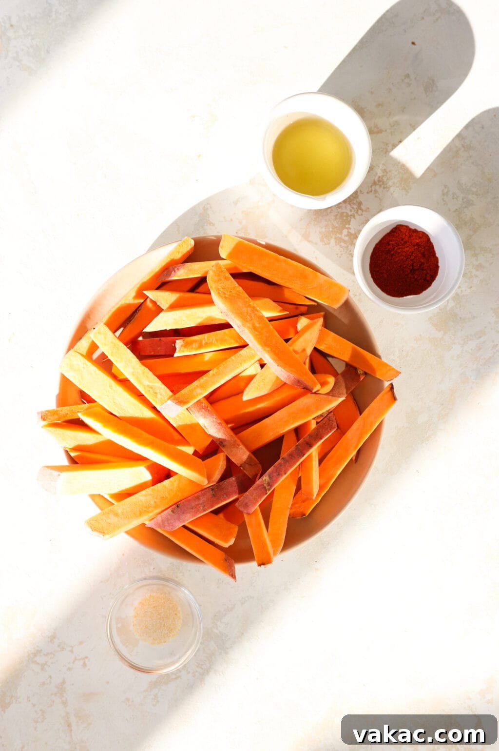 The Ultimate 4-Ingredient Crispy Air Fryer Sweet Potato Wedges 3 Simple ingredients laid out for air fryer sweet potato wedges: sliced sweet potatoes, a bottle of avocado oil, red paprika, and a shaker of garlic salt.