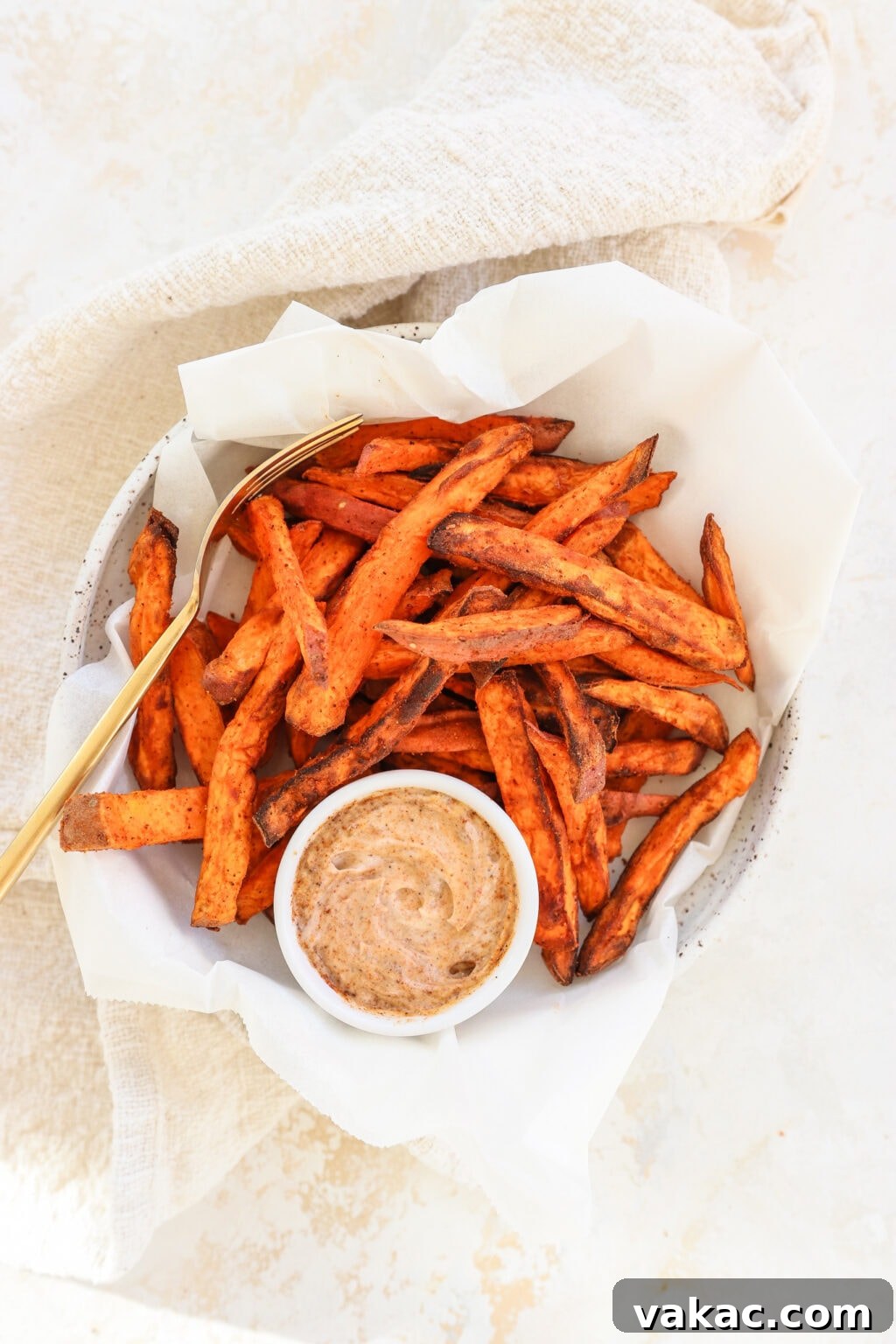 The Ultimate 4-Ingredient Crispy Air Fryer Sweet Potato Wedges 6 Crispy air fryer sweet potato wedges in a white bowl, served on parchment paper with a side of dipping sauce.
