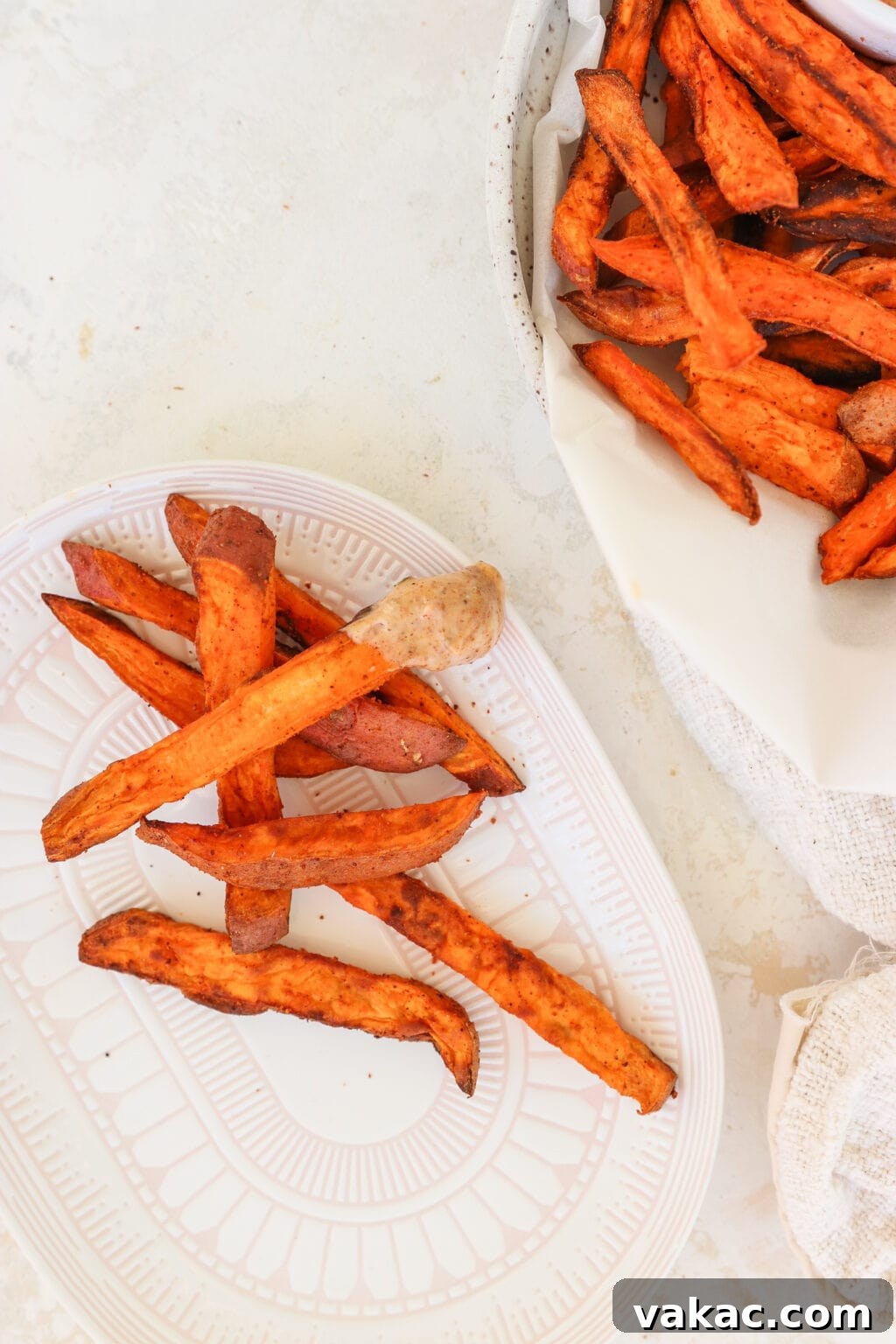 The Ultimate 4-Ingredient Crispy Air Fryer Sweet Potato Wedges 8 Crispy air fryer sweet potato wedges presented attractively in a white bowl, with a few extra wedges artfully placed on a small white plate.