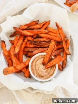 4 Ingredient Crispy Air Fryer Sweet Potato Wedges in a white bowl with parchment paper and dip on the side