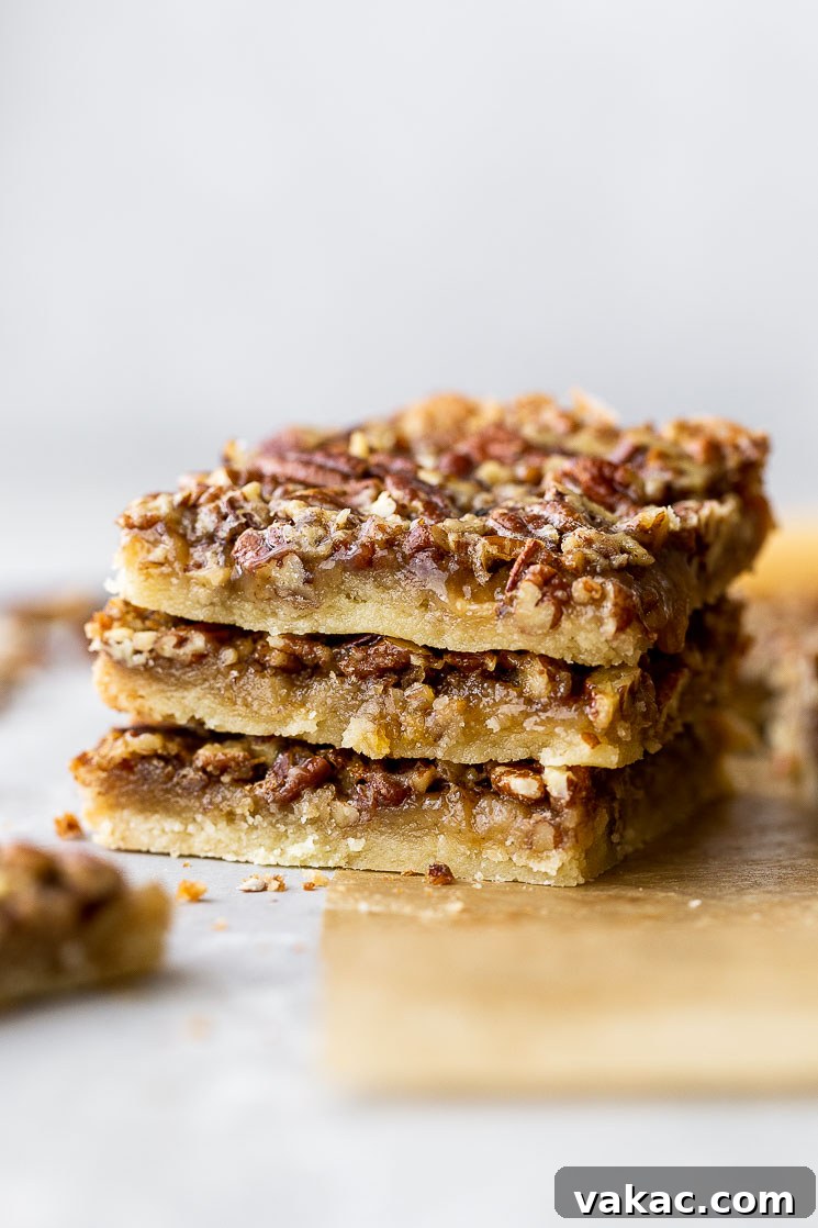 A stack of three golden brown pecan pie bars on rustic brown parchment paper, showcasing the rich pecan topping and the sturdy shortbread base.