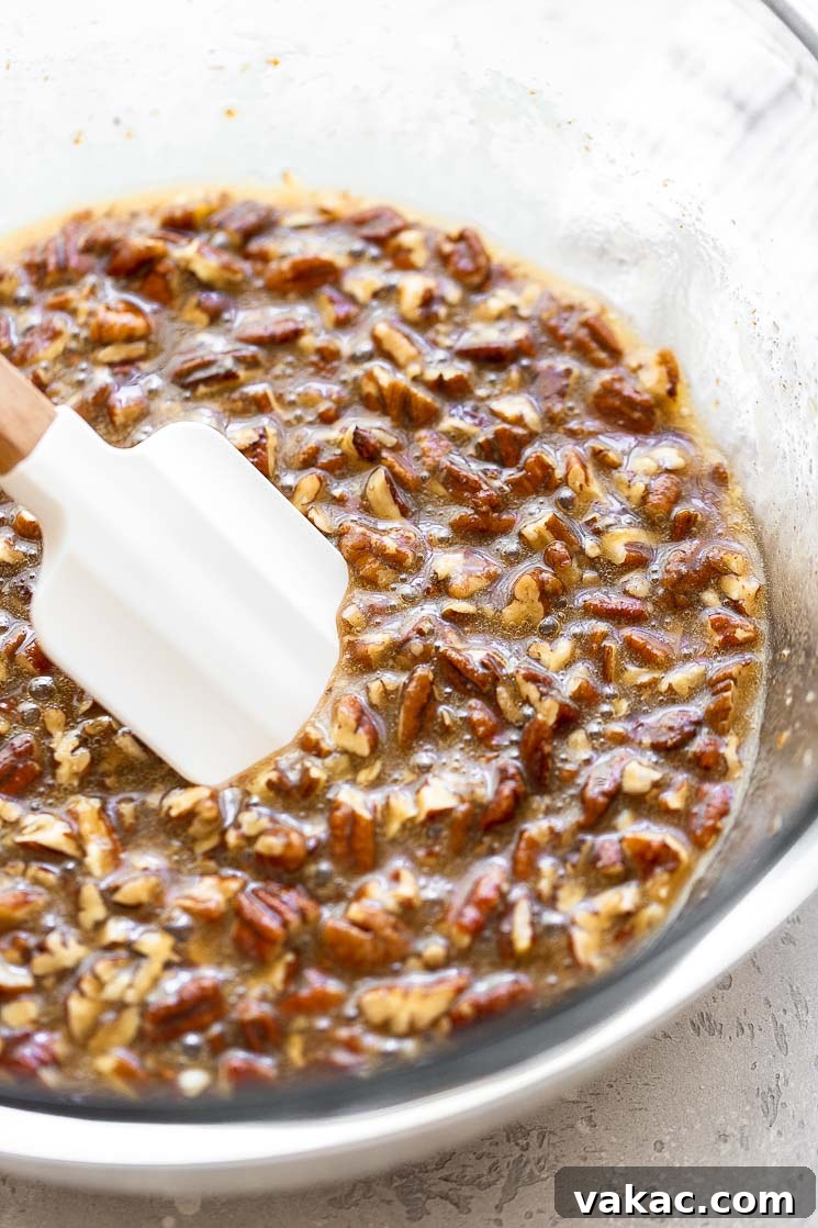 Pecan pie filling in a glass mixing bowl, showcasing the rich, gooey texture with chopped pecans.