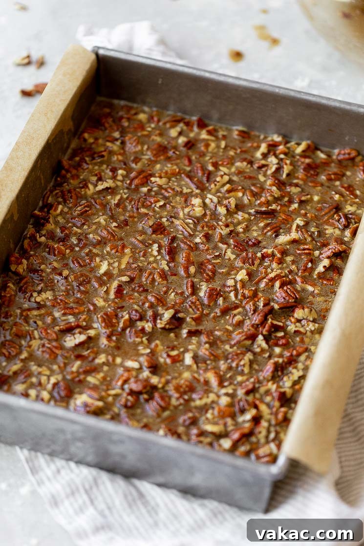 The pecan pie filling being carefully poured and spread on top of the golden shortbread crust in a baking pan.