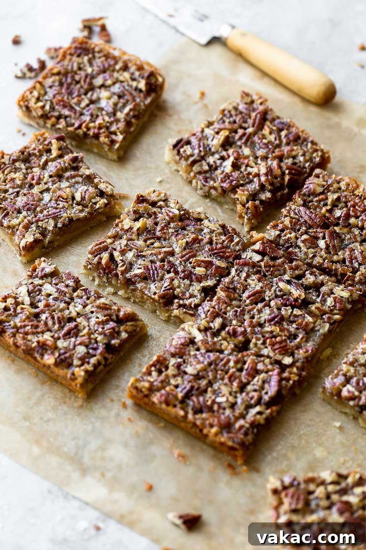 A cutting board with sliced Pecan Pie Bars arranged on parchment paper, with a knife in the background, ready for serving.