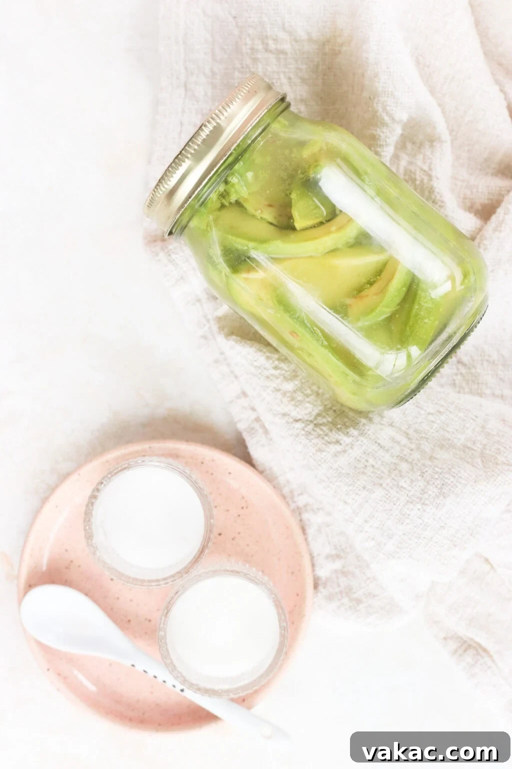 Rapid Tangy Avocados from the Jar 2 Quick pickled avocados in a glass jar, perfectly sliced and submerged in brine, with a decorative pink plate nearby