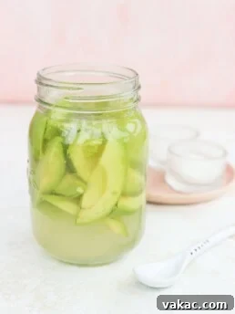 Quick pickled avocados in a glass jar with a pink plate beside it