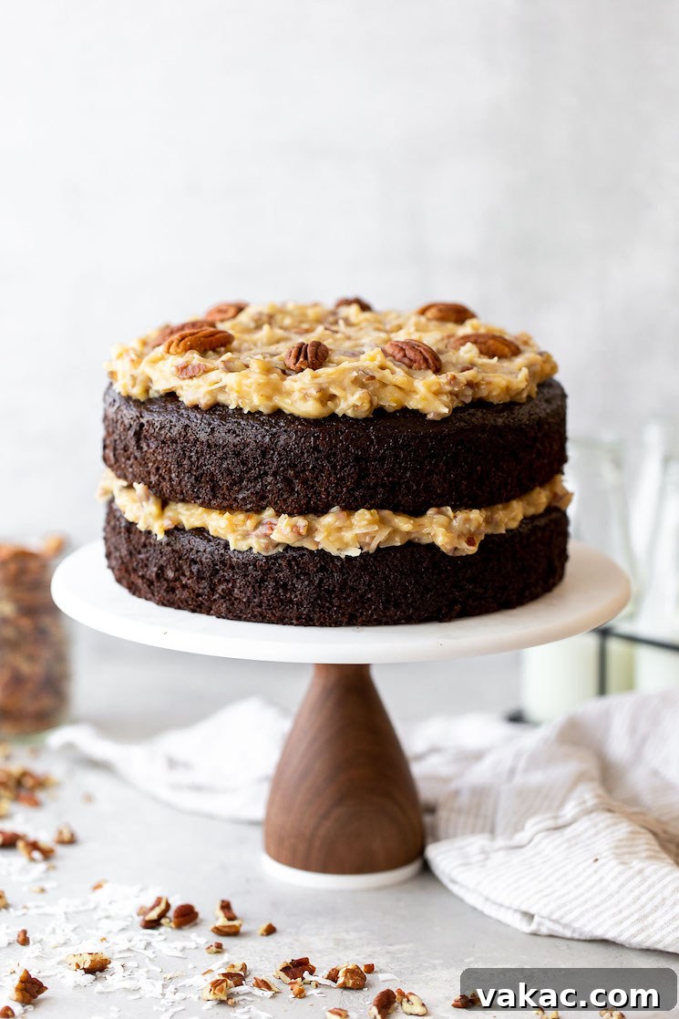 Signature German Chocolate Creation 2 A layered German Chocolate Cake on a marble cake stand with chopped pecans and coconut around it.