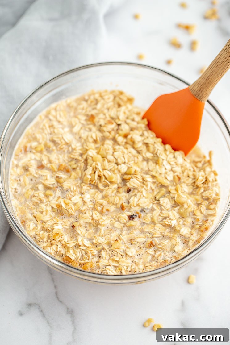 A glass mixing bowl holds a creamy, golden banana oatmeal mixture, ready for the next step in preparing the baked oatmeal cups.