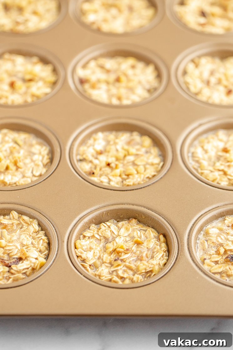A copper-colored muffin pan filled with the banana oatmeal mixture, perfectly portioned and ready to be placed into the oven for baking.