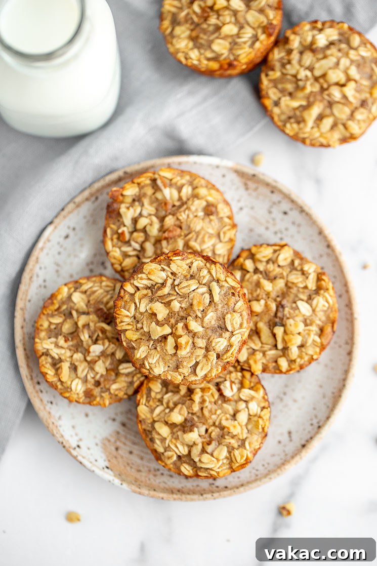 A speckled ceramic plate holds two banana baked oatmeal cups, resting on a clean marble surface, with more oatmeal cups and a glass of milk blurred in the background, suggesting a delightful breakfast scene.