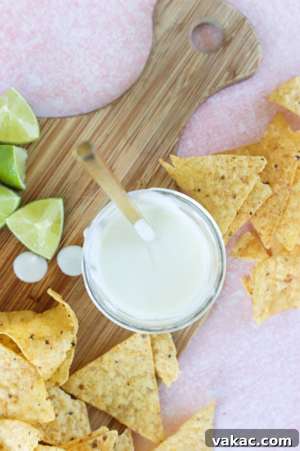 Just 4 Ingredients for Tangy Greek Yogurt Lime Crema 2 Creamy Greek Yogurt Lime Crema in a white bowl, served on a butcher block with tortilla chips and fresh lime wedges on the side, ready to be enjoyed.