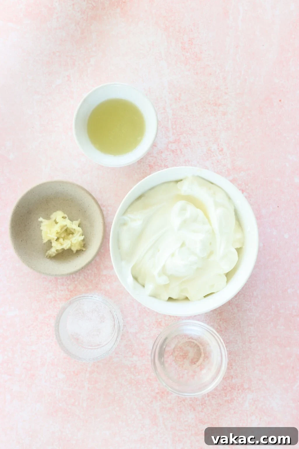 Just 4 Ingredients for Tangy Greek Yogurt Lime Crema 3 Individual white bowls showcasing the simple ingredients for Greek Yogurt Lime Crema: plain Greek yogurt, fresh lime juice, warm water, minced garlic, and a pinch of salt, arranged on a pink countertop.