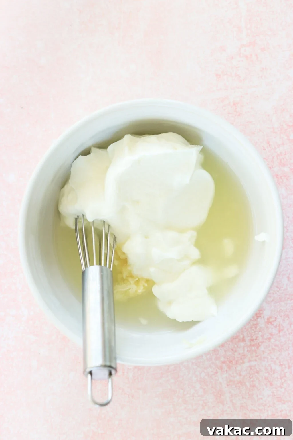 Just 4 Ingredients for Tangy Greek Yogurt Lime Crema 4 All ingredients for Greek Yogurt Lime Crema combined in a white bowl with a metal whisk resting in it, on a bright pink countertop, illustrating the first step of mixing.