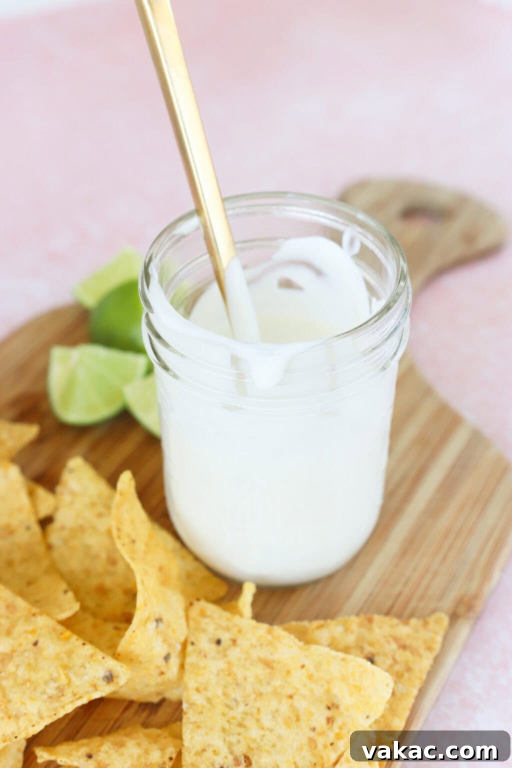 Just 4 Ingredients for Tangy Greek Yogurt Lime Crema 6 The finished Greek Yogurt Lime Crema in a white serving bowl, presented on a rustic butcher block with a scattering of tortilla chips and lime wedges, showcasing the final product.