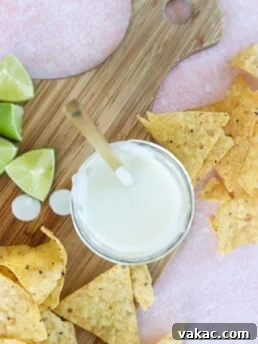 Creamy Greek Yogurt Lime Crema in a white bowl, served on a butcher block with tortilla chips and fresh lime wedges.
